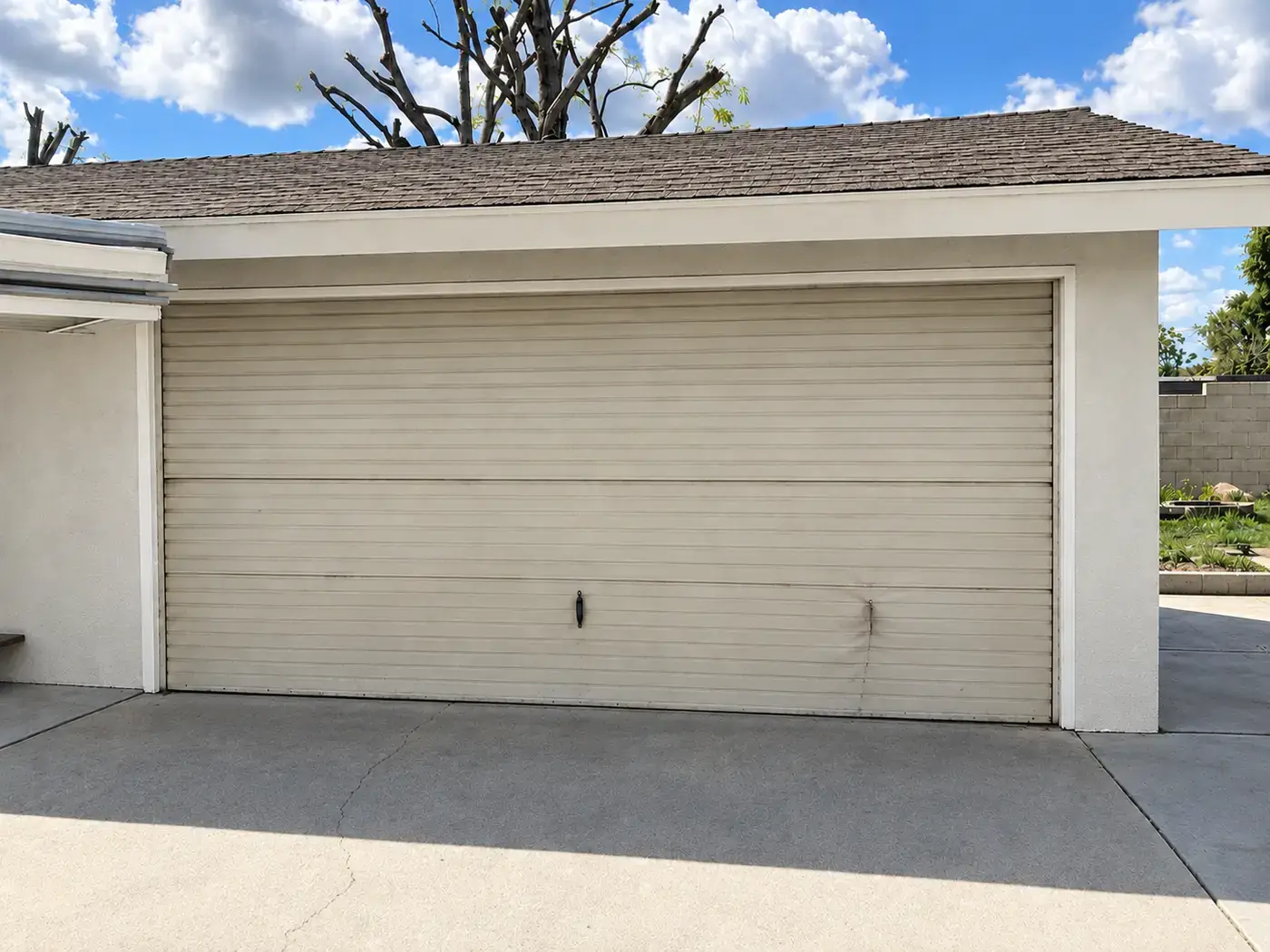 Before, older tan steel garage door with a dented panel.